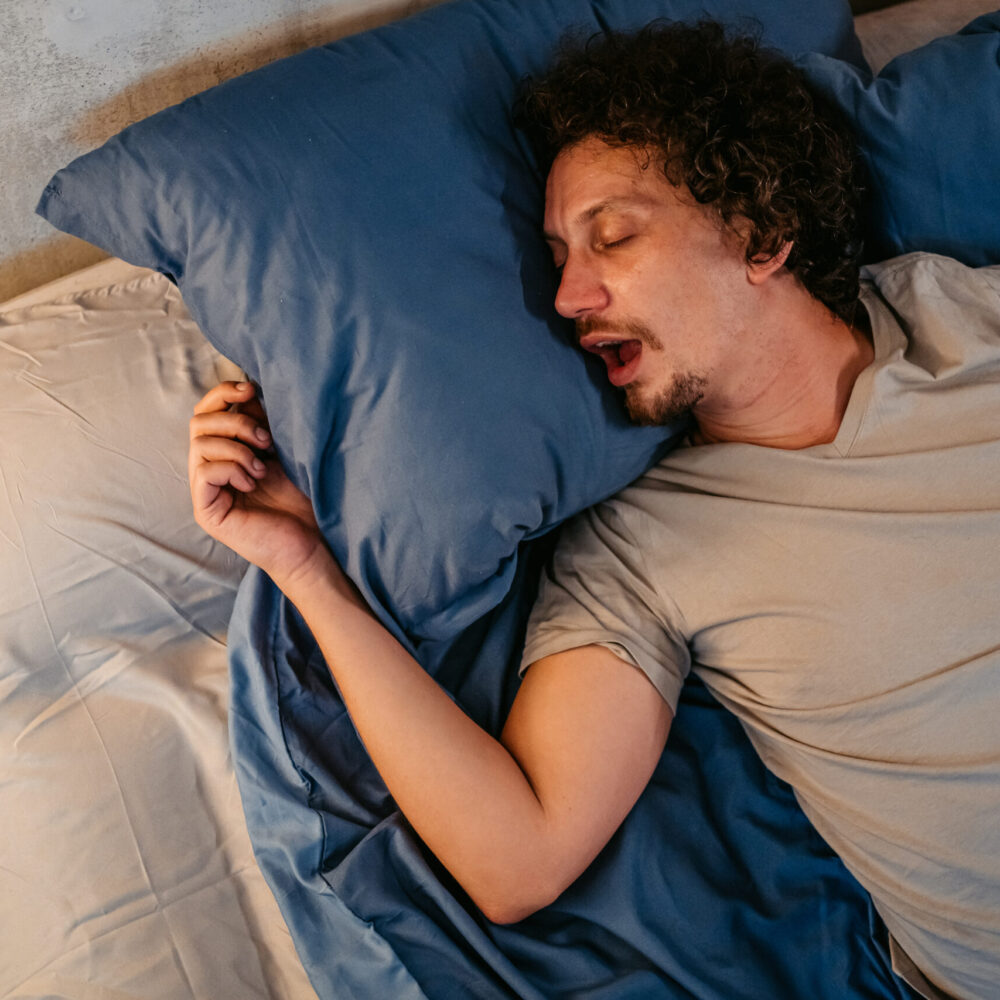 Handsome young man sleeping in the bed at night in his bedroom. Snoring and having breathing problems.